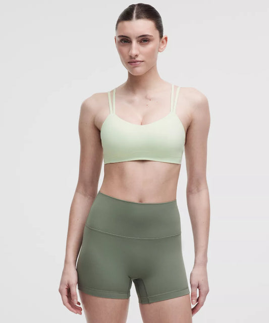Woman wearing a light green sports bra and olive green shorts on a white background