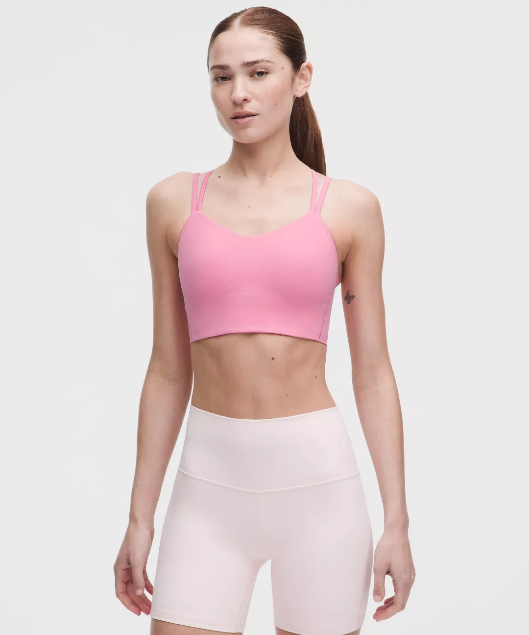 Woman wearing a pink sports bra and white shorts on a light gray background