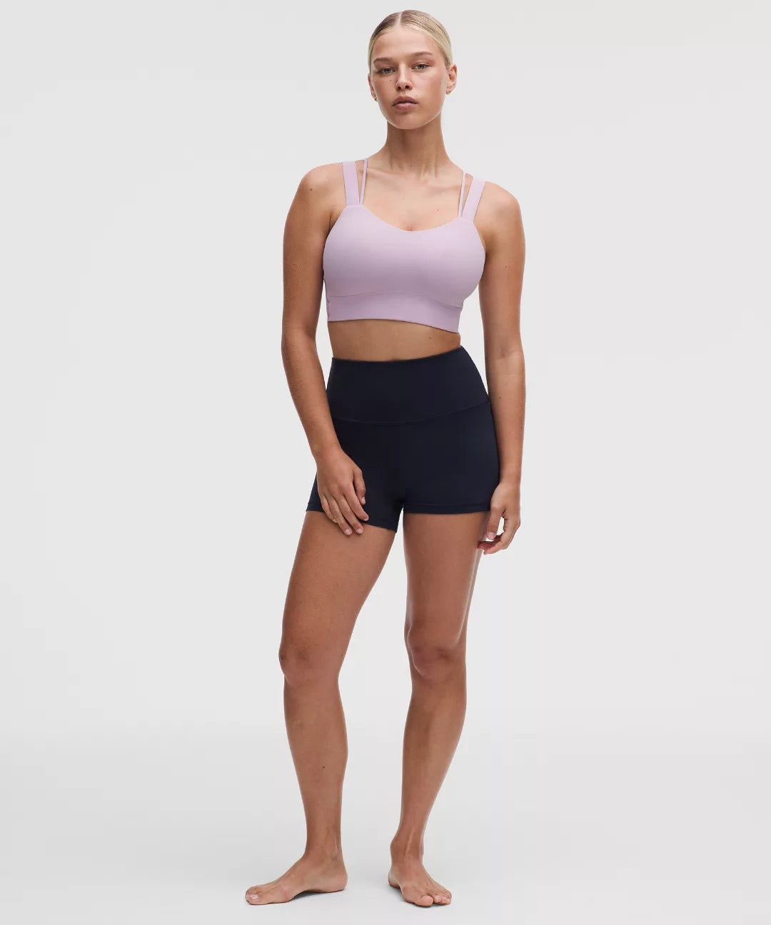 Woman wearing a light purple sports bra and black shorts on a white background