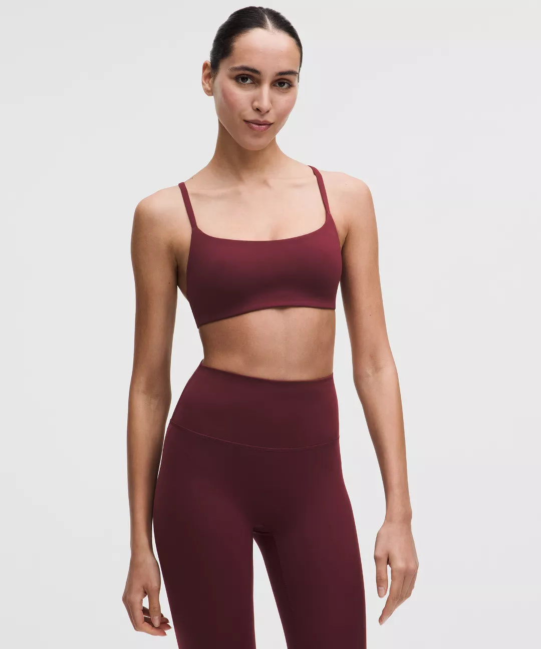 Woman wearing a maroon sports bra and leggings on a light gray background