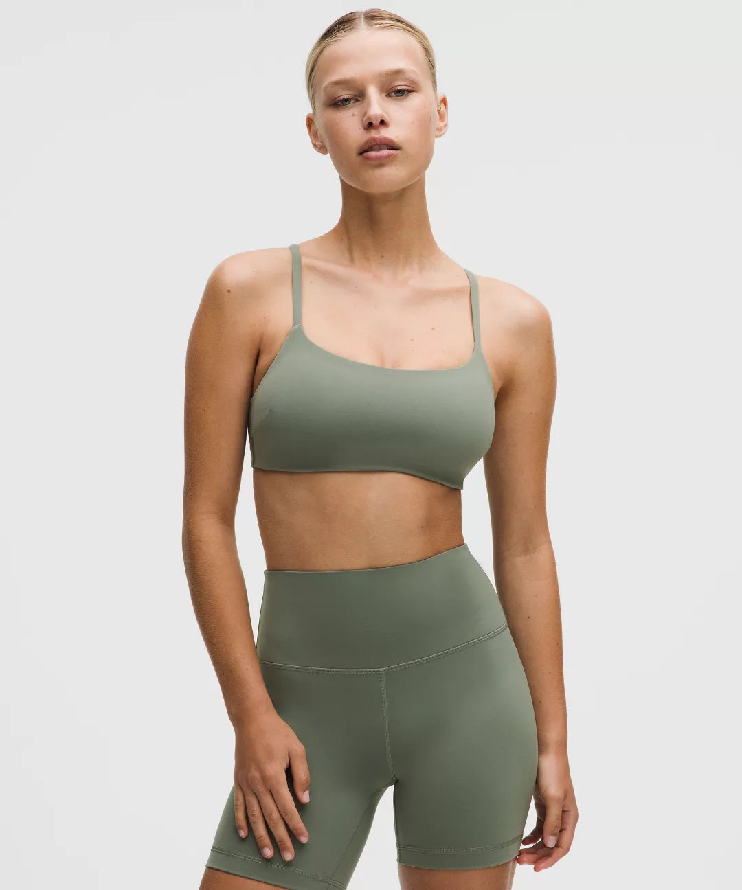 Woman wearing a green sports bra and shorts set on a light gray background