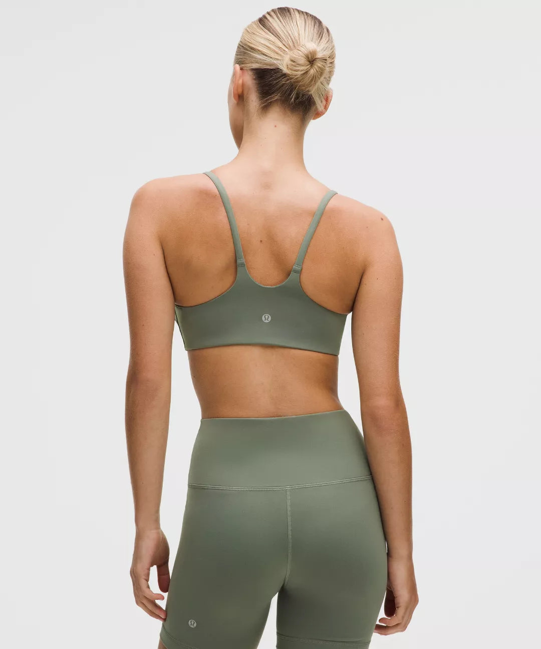 Person wearing a green sports bra and leggings set on a light gray background