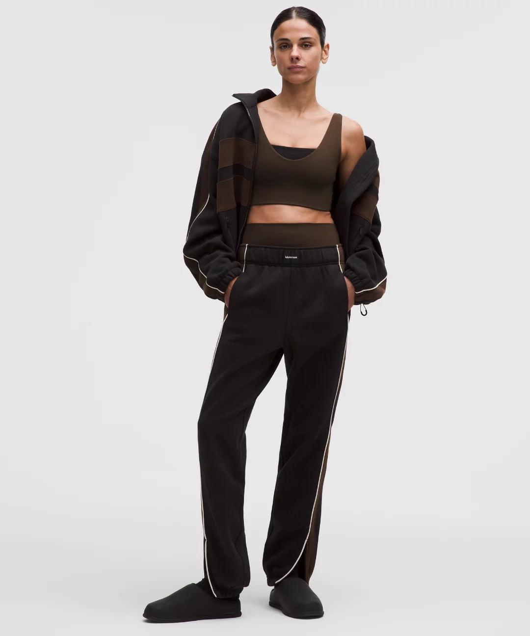Person wearing a brown sports bra and black pants with white stripes on a white background