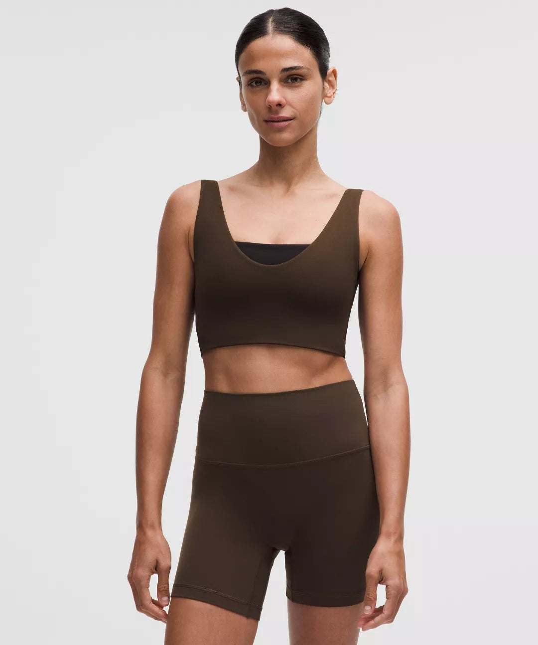 Woman wearing a brown sports bra and shorts set on a light gray background