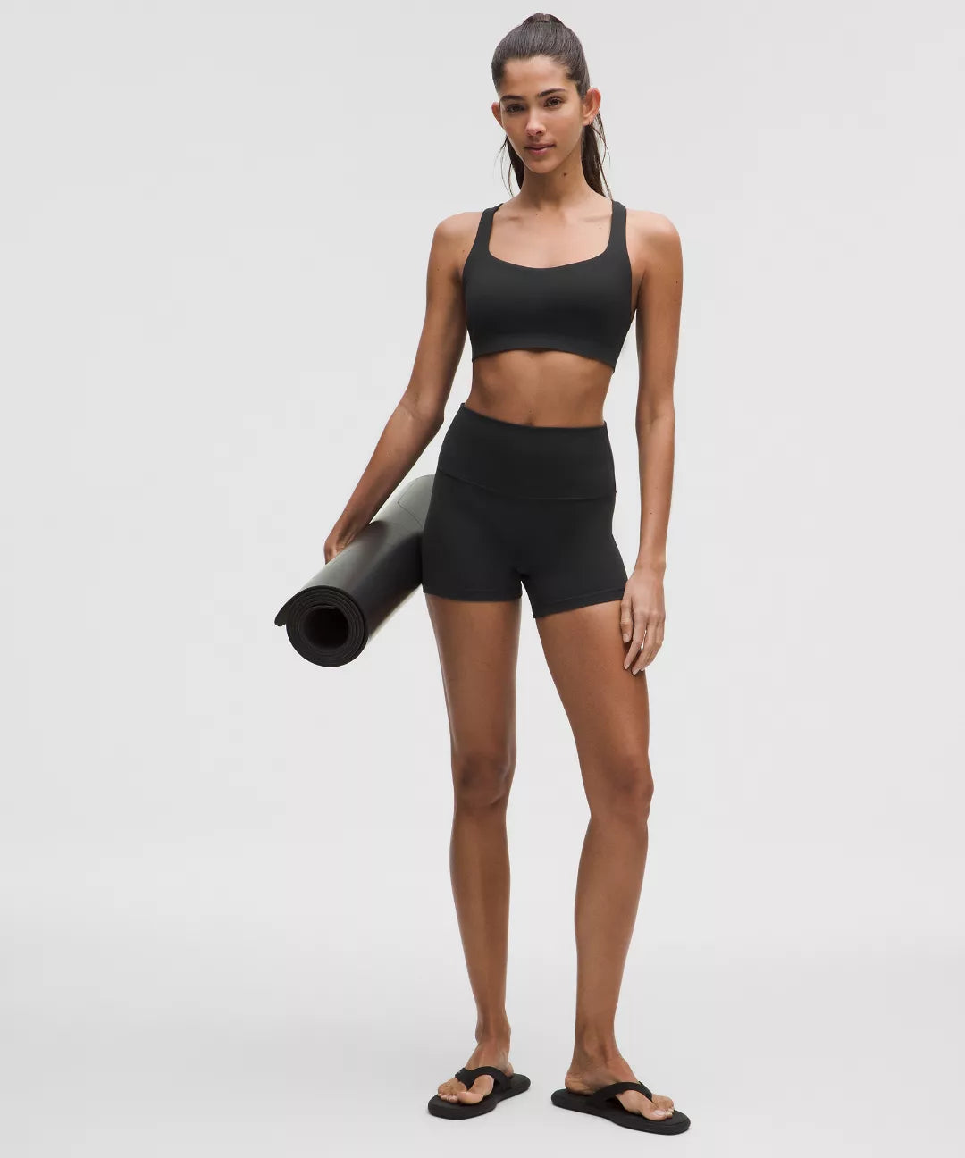 Woman in black athletic wear holding a yoga mat on a white background