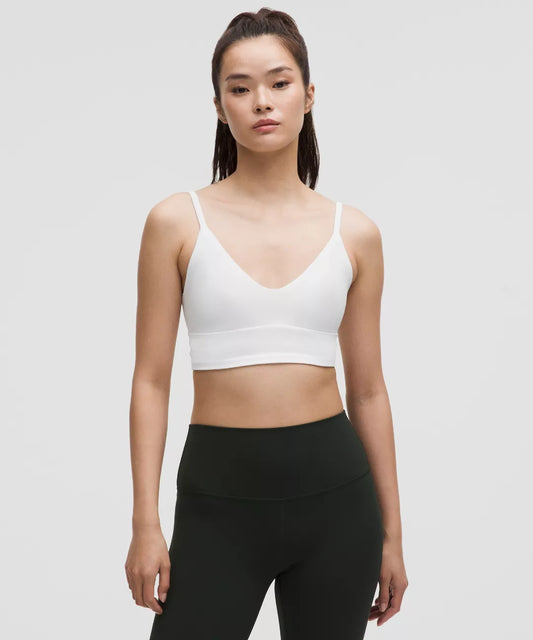 Woman wearing a white sports bra and black leggings on a light gray background