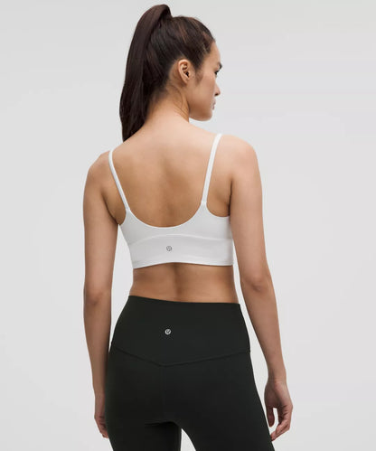 Woman wearing a white sports bra and black leggings on a light gray background