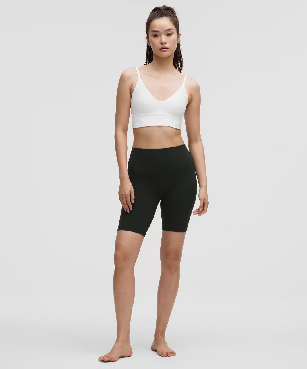 Woman wearing a white sports bra and black shorts on a plain background