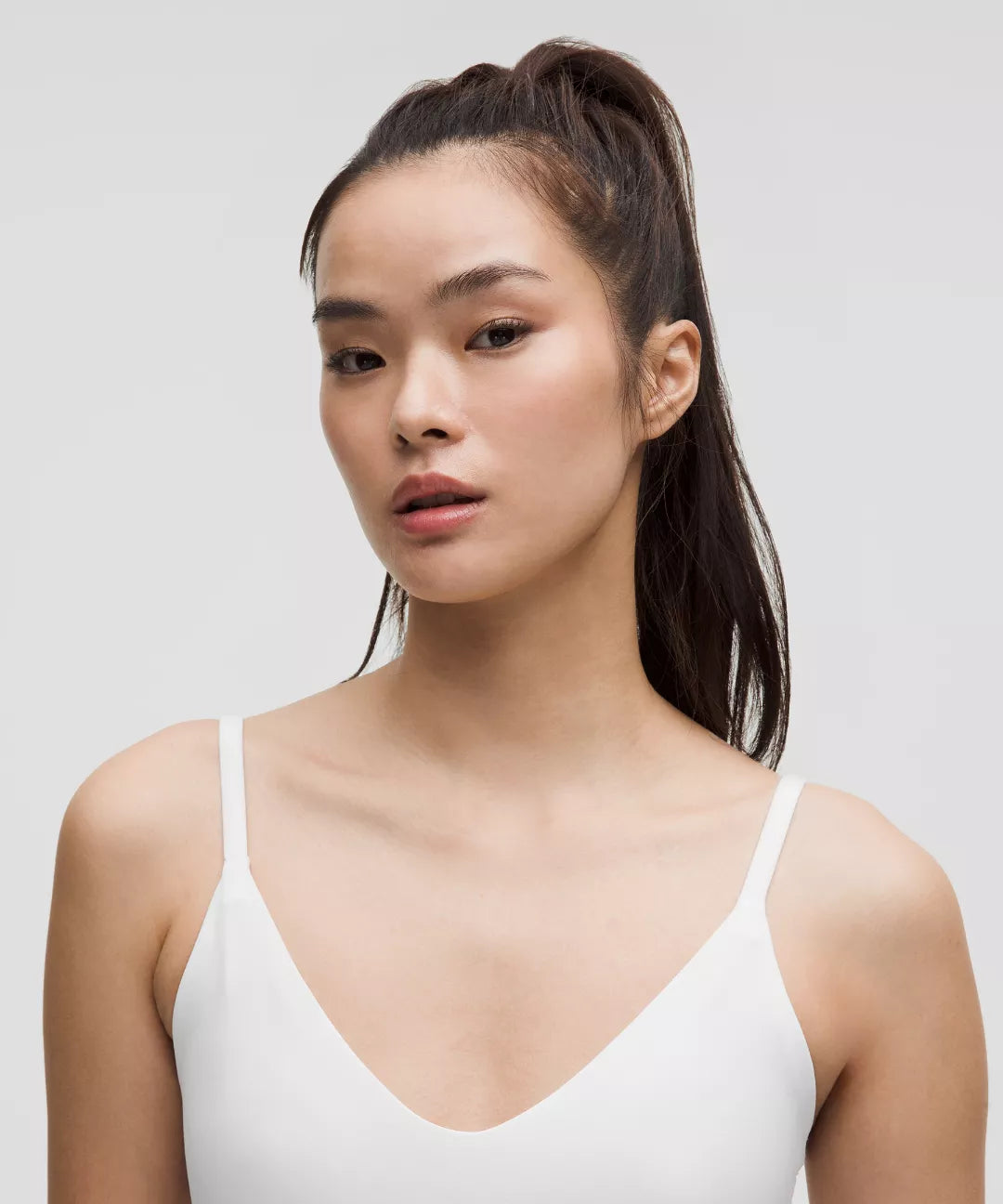 Woman wearing a white tank top against a plain background