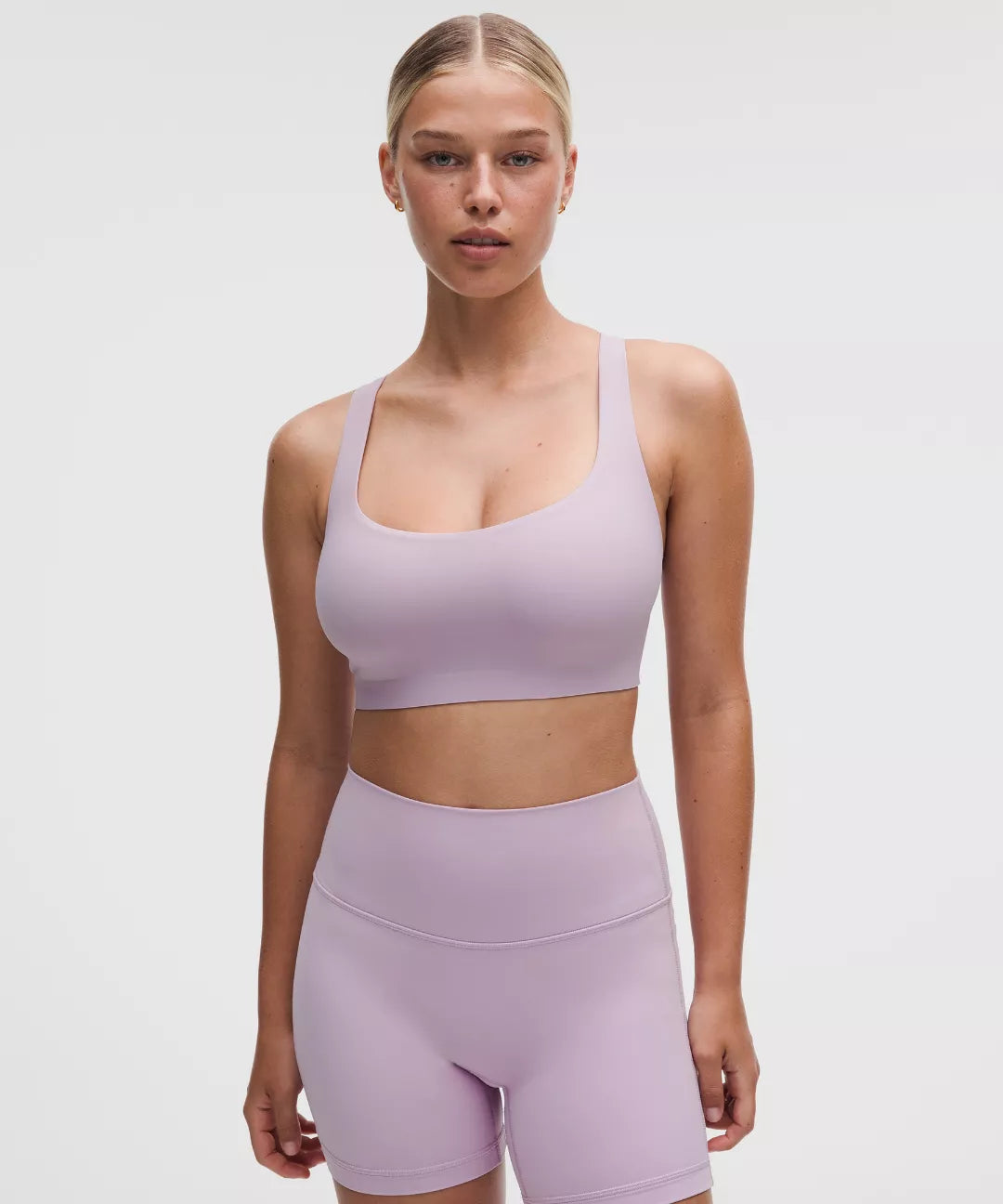 Woman wearing a lavender sports bra and shorts on a white background