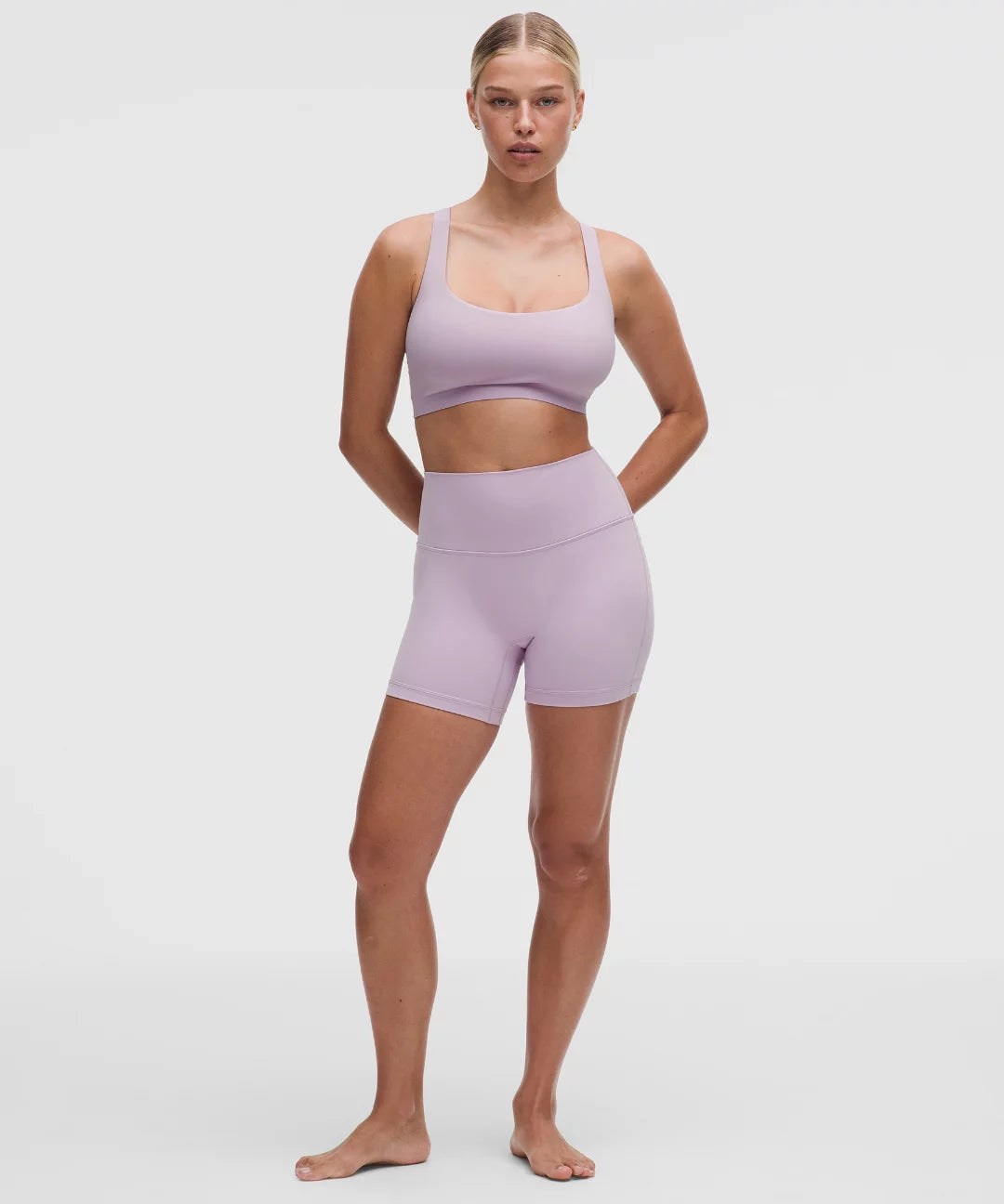 Woman wearing a lavender sports bra and shorts set on a white background