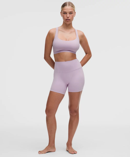 Woman wearing a lavender sports bra and shorts set on a white background