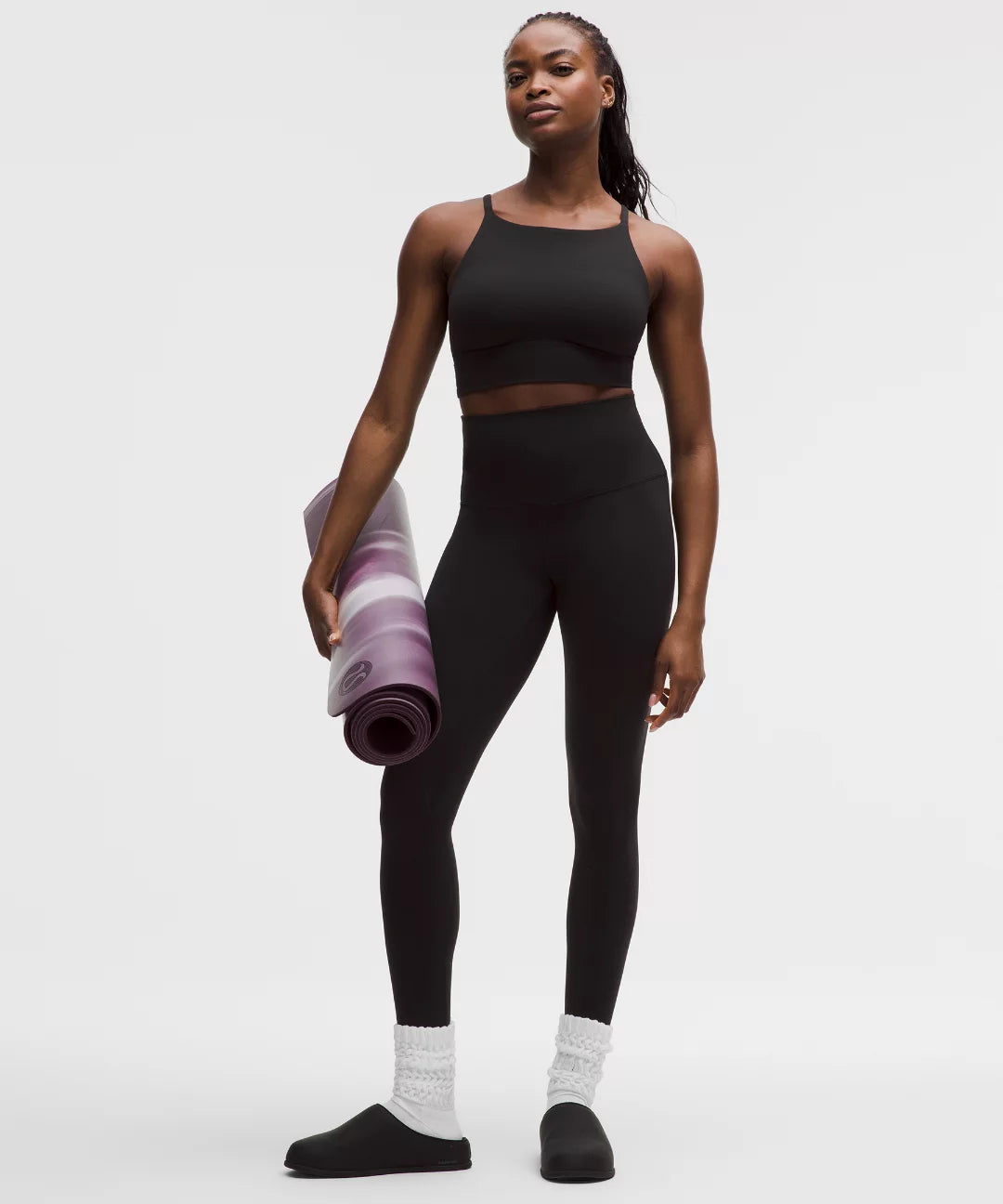 Woman in black athletic wear holding a purple yoga mat on a white background