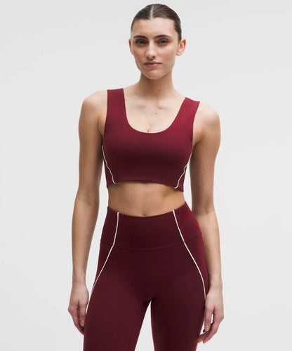 Woman wearing a maroon sports bra and leggings set on a light gray background