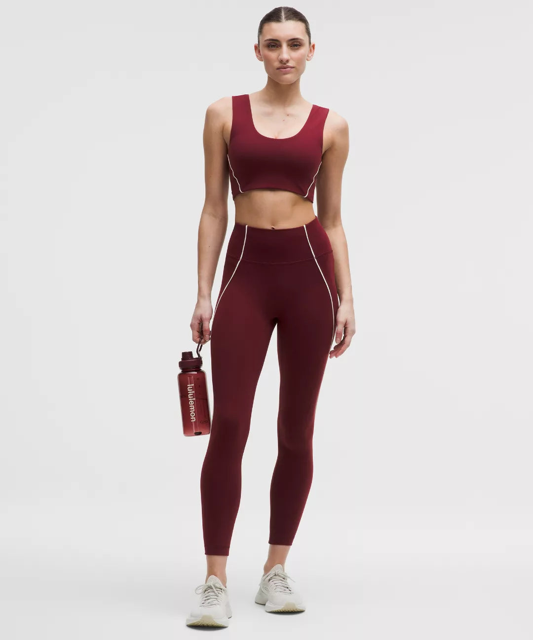 Woman wearing a maroon athletic outfit holding a water bottle on a white background