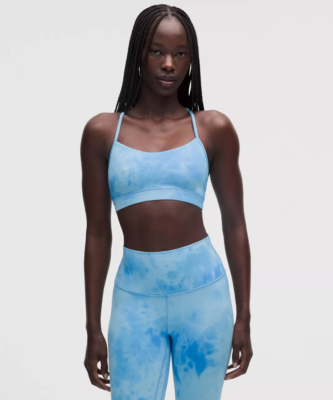Woman wearing a blue tie-dye sports bra and leggings set on a light gray background