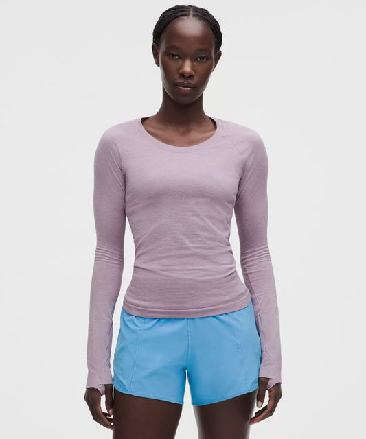 Woman wearing a purple long-sleeve top and blue shorts on a white background
