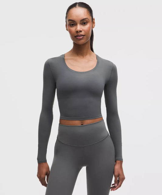 Woman wearing a gray long-sleeve top and leggings on a light gray background