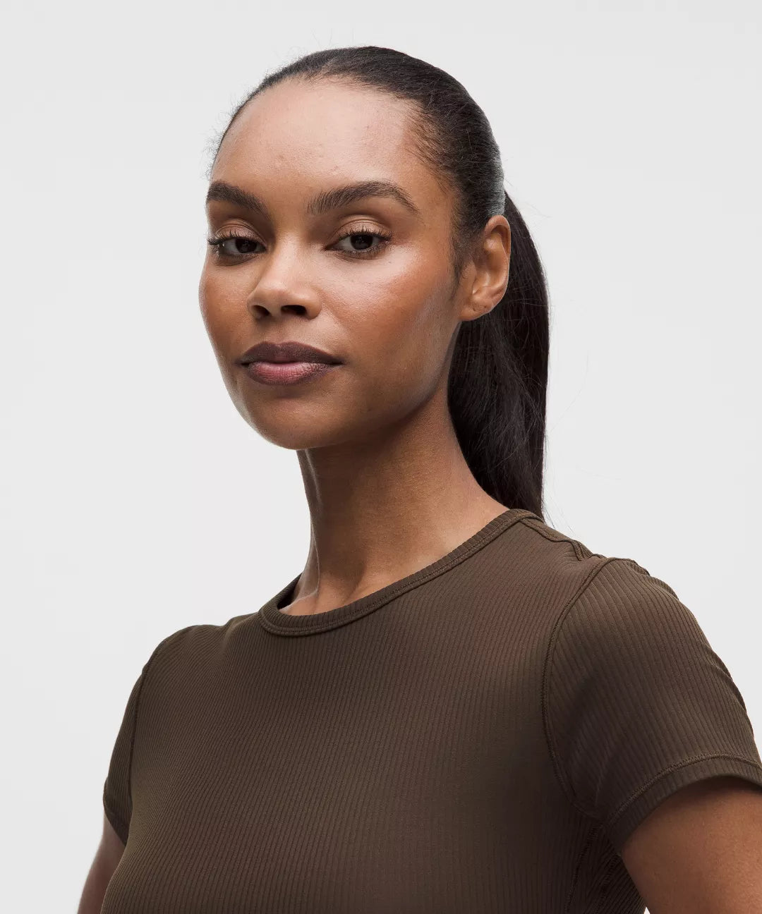 Woman wearing a brown ribbed t-shirt against a plain background