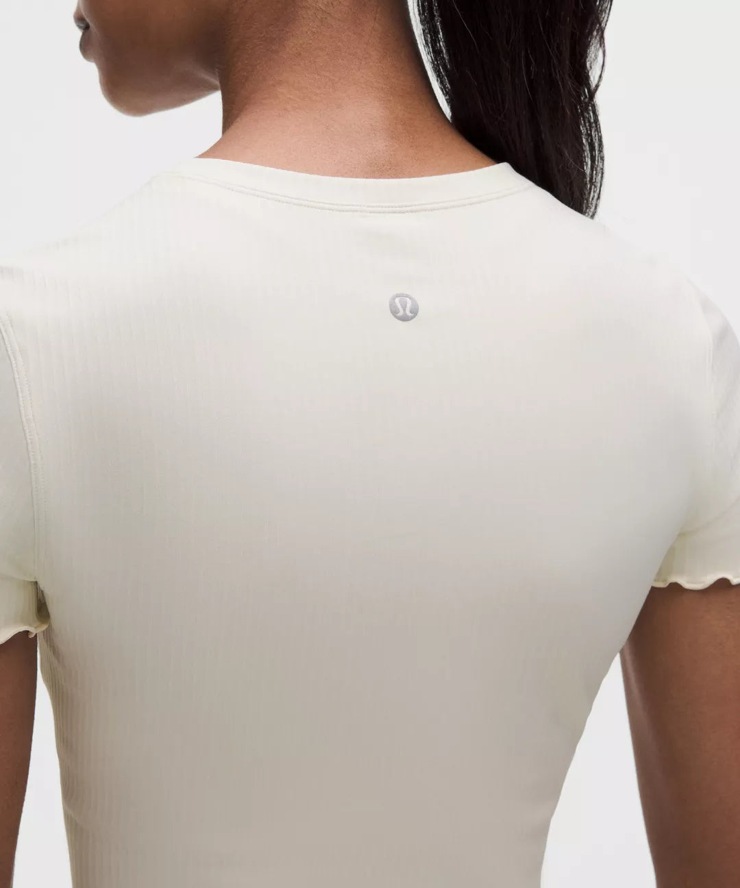 Close-up of a person wearing a beige t-shirt with a brand logo on the chest.