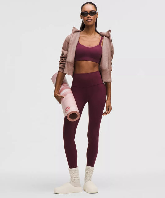Woman in maroon athletic wear holding a pink yoga mat on a white background