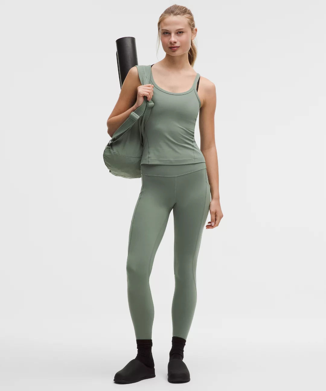 Woman in green athletic wear holding a yoga mat on a white background