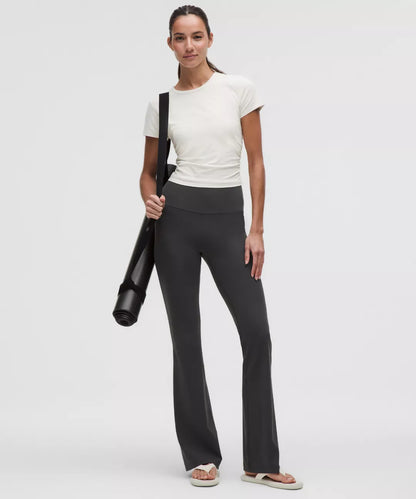 Woman holding a yoga mat wearing a white shirt and black pants on a white background