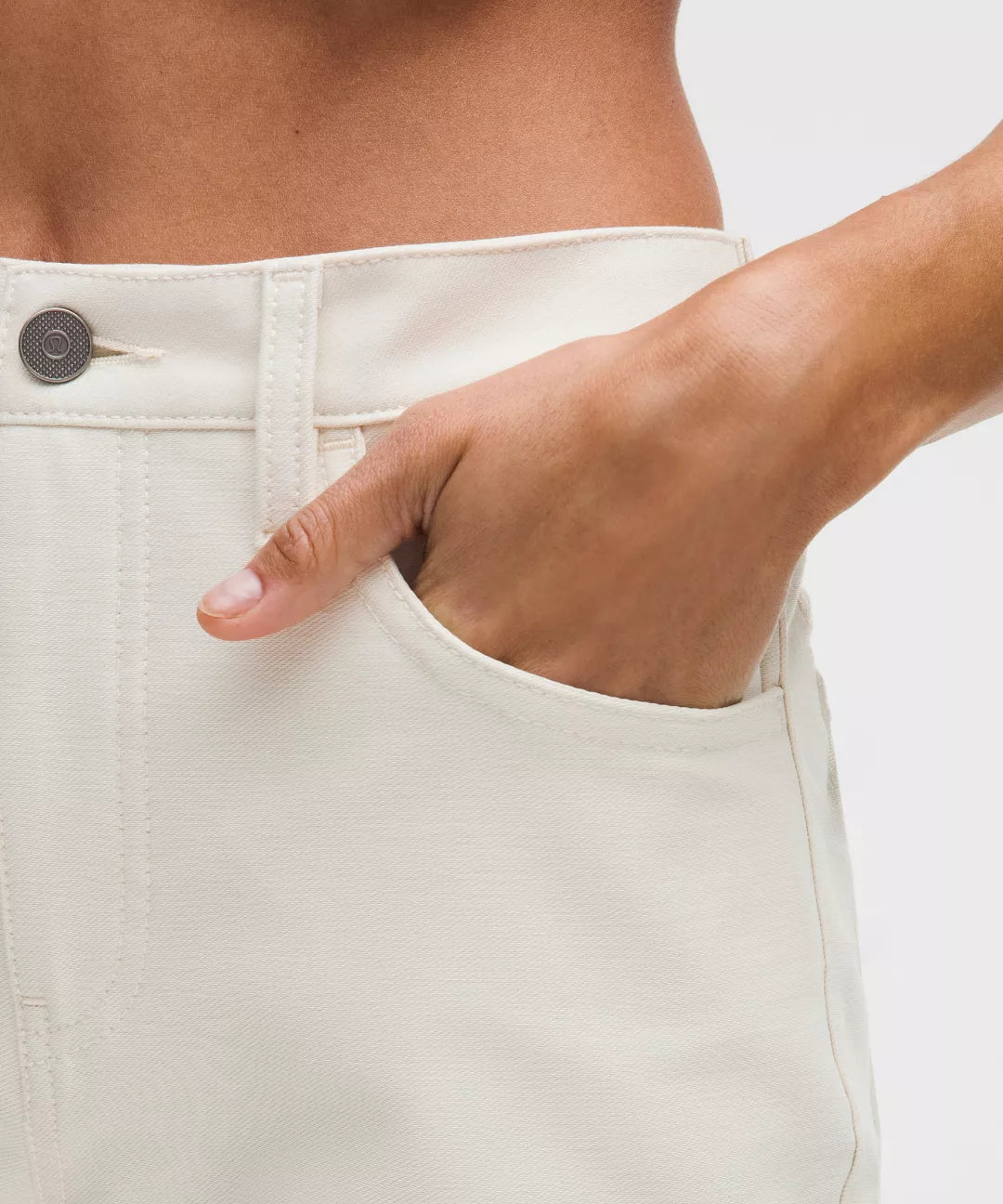 Close-up of a person wearing white pants with a hand in the pocket against a light background