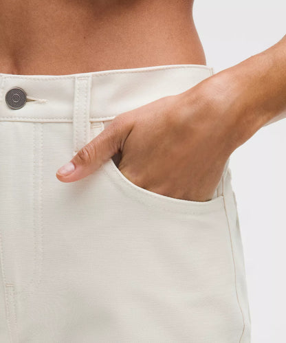 Close-up of a person wearing white pants with a hand in the pocket against a light background