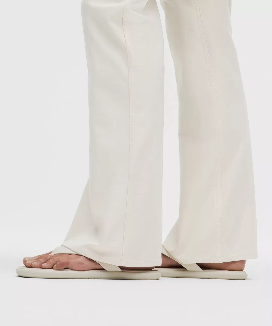 Person wearing white sandals and pants on a plain background