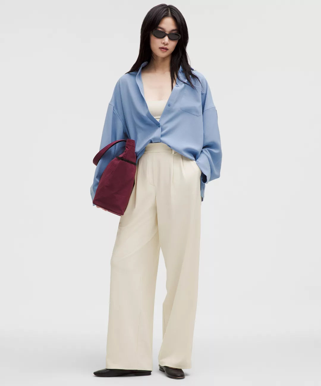 Person wearing a light blue shirt, beige pants, and dark sunglasses on a white background