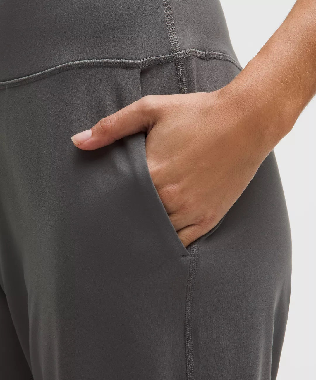 Person wearing gray pants with a hand in one of the pockets on a white background