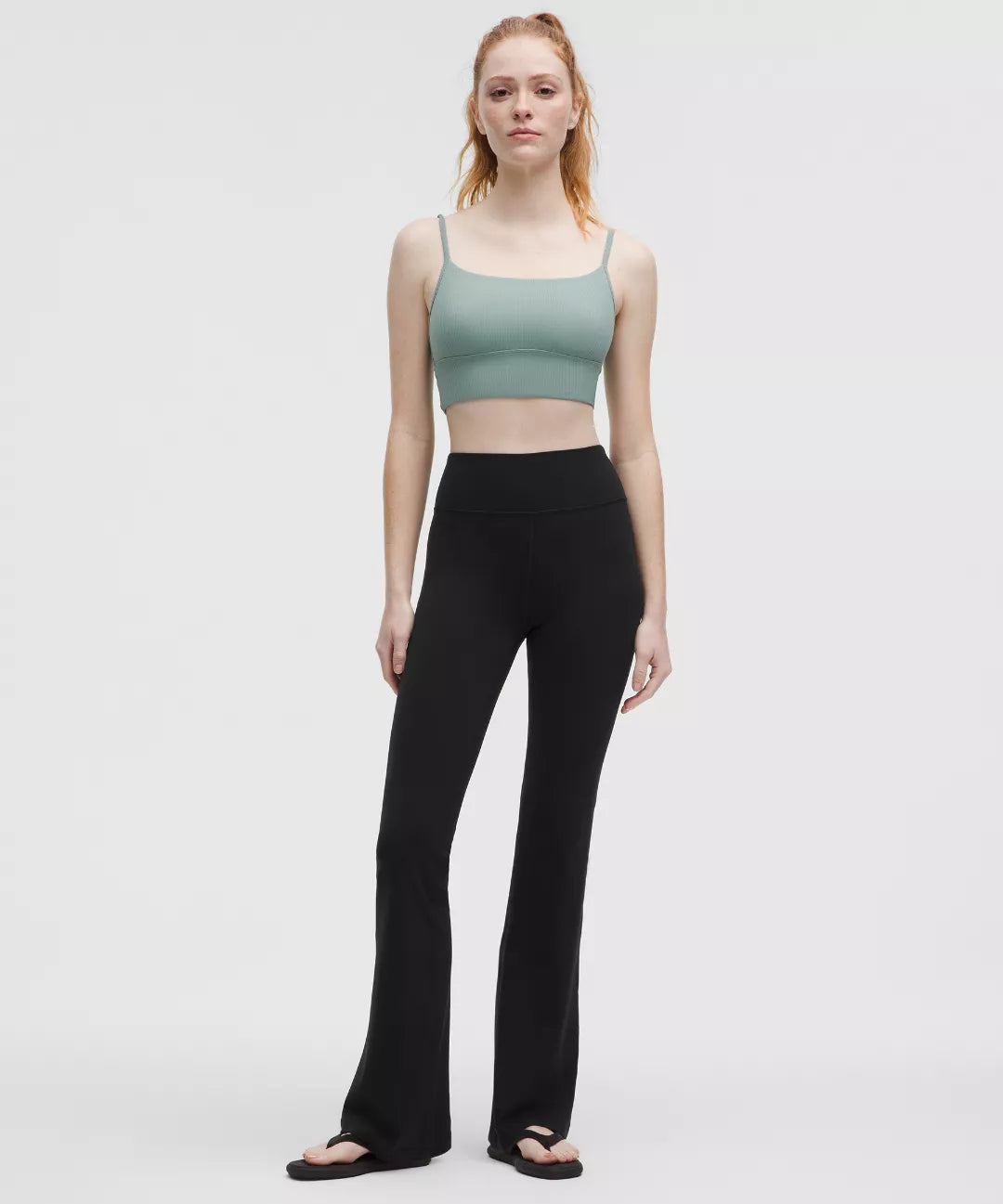 Woman wearing a green sports bra and black leggings on a white background