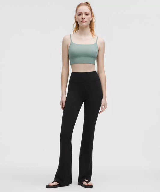Woman wearing a green sports bra and black leggings on a white background