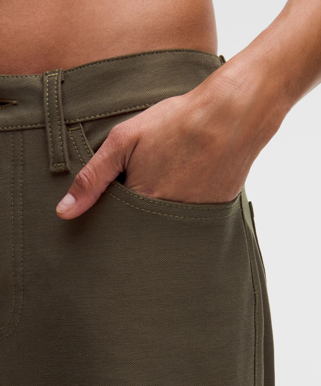 Person wearing olive green pants with a hand in the pocket on a light gray background