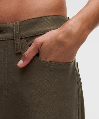 Person wearing olive green pants with a hand in the pocket on a light gray background
