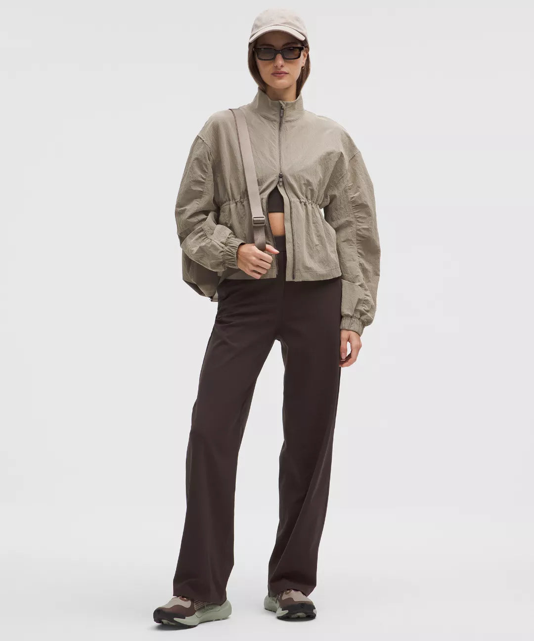 Person wearing a beige jacket and dark pants on a white background