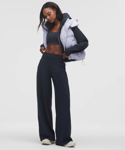 Woman wearing a black puffer jacket, gray top, and dark pants on a white background