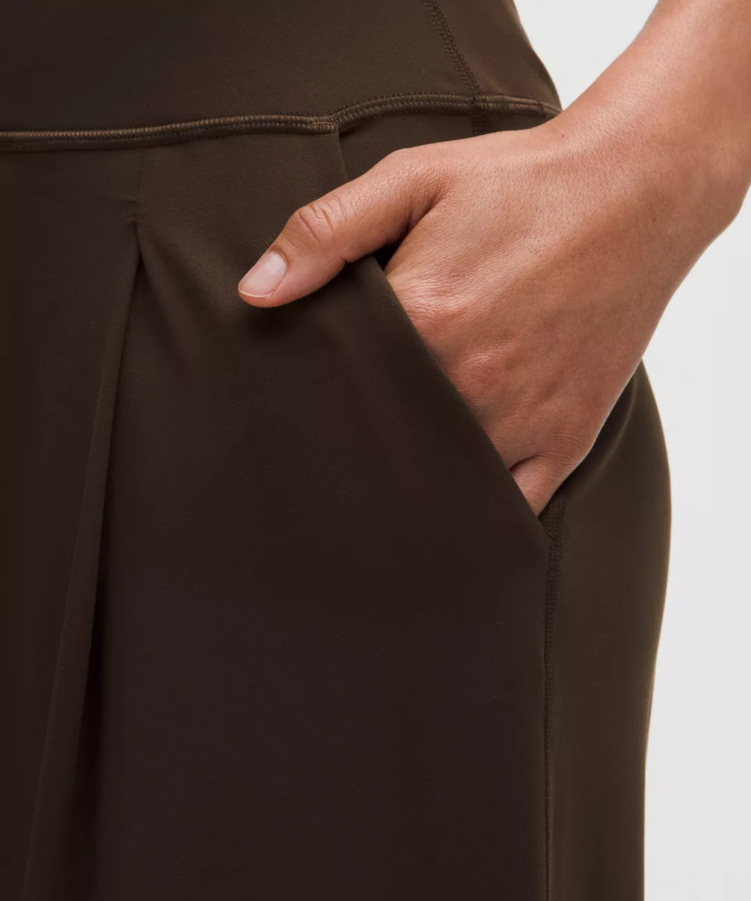 Brown pants with a hand in the pocket against a neutral background