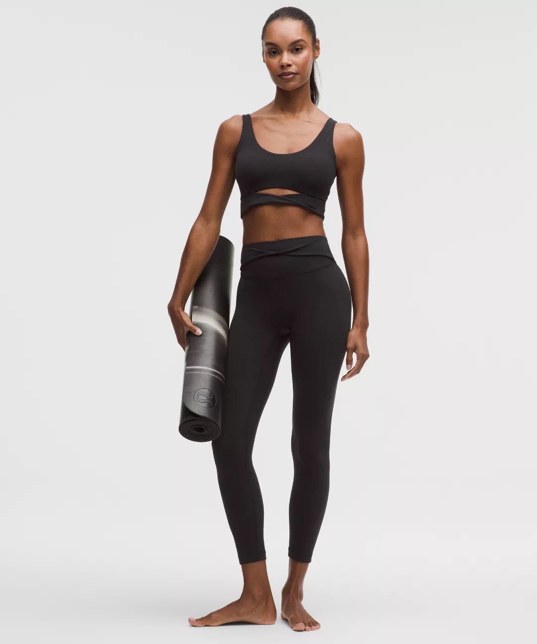 Woman in black athletic wear holding a yoga mat on a white background