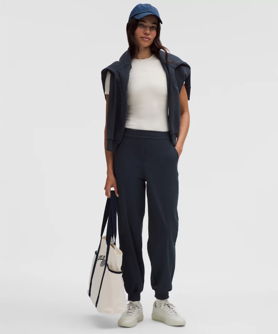 Person wearing a navy outfit with a white top, holding a white bag on a light gray background