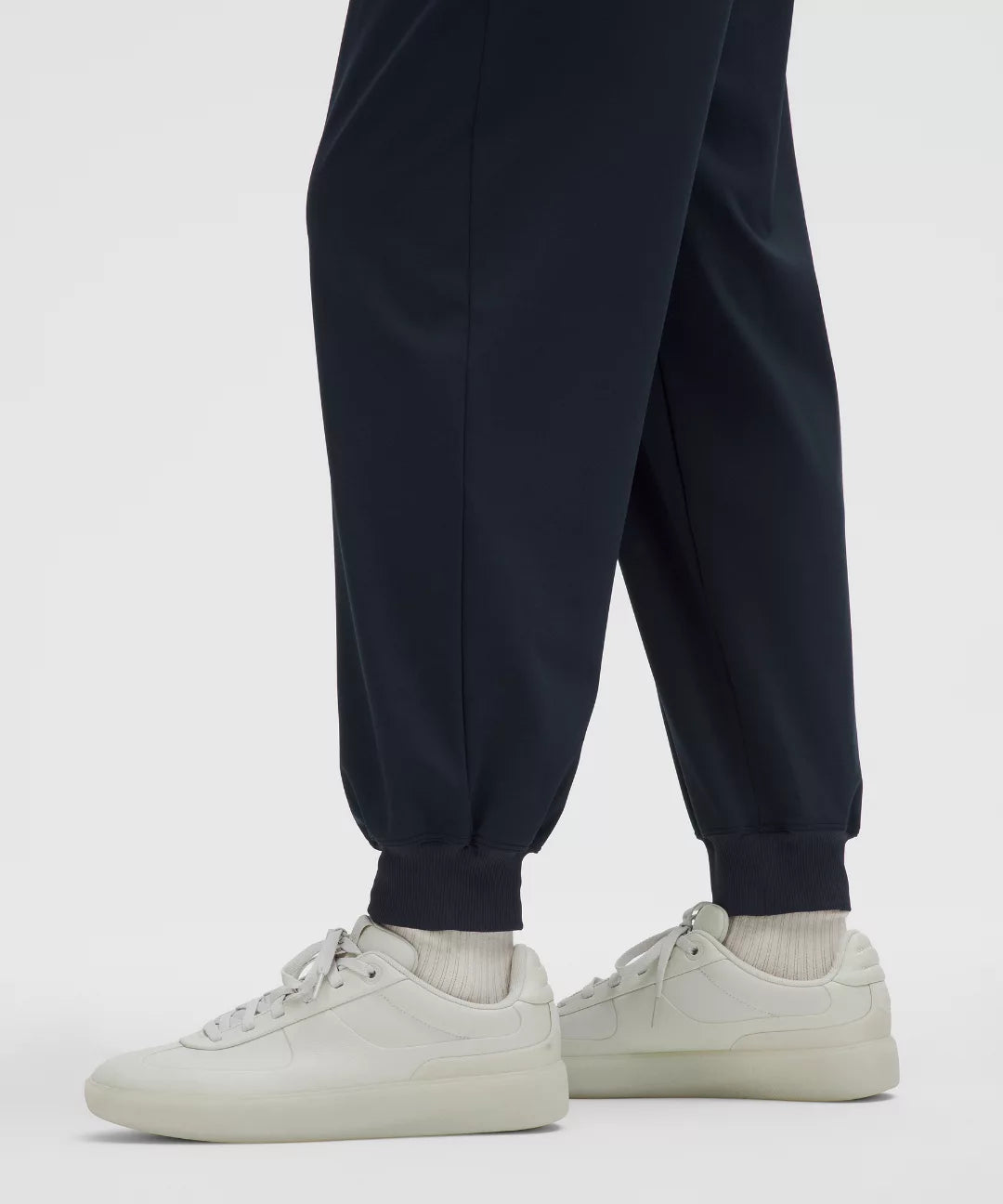 Person wearing navy jogger pants and white sneakers on a light gray background