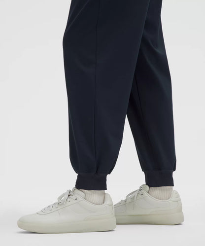 Person wearing navy jogger pants and white sneakers on a light gray background