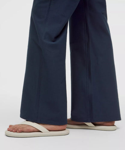 Navy blue wide-leg pants worn with white sandals on a light gray background