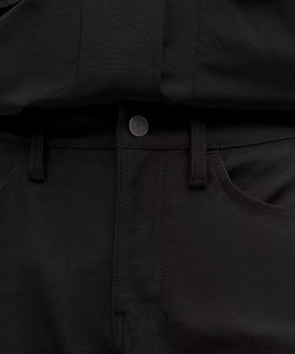 Close-up of black pants with a button and belt buckle.