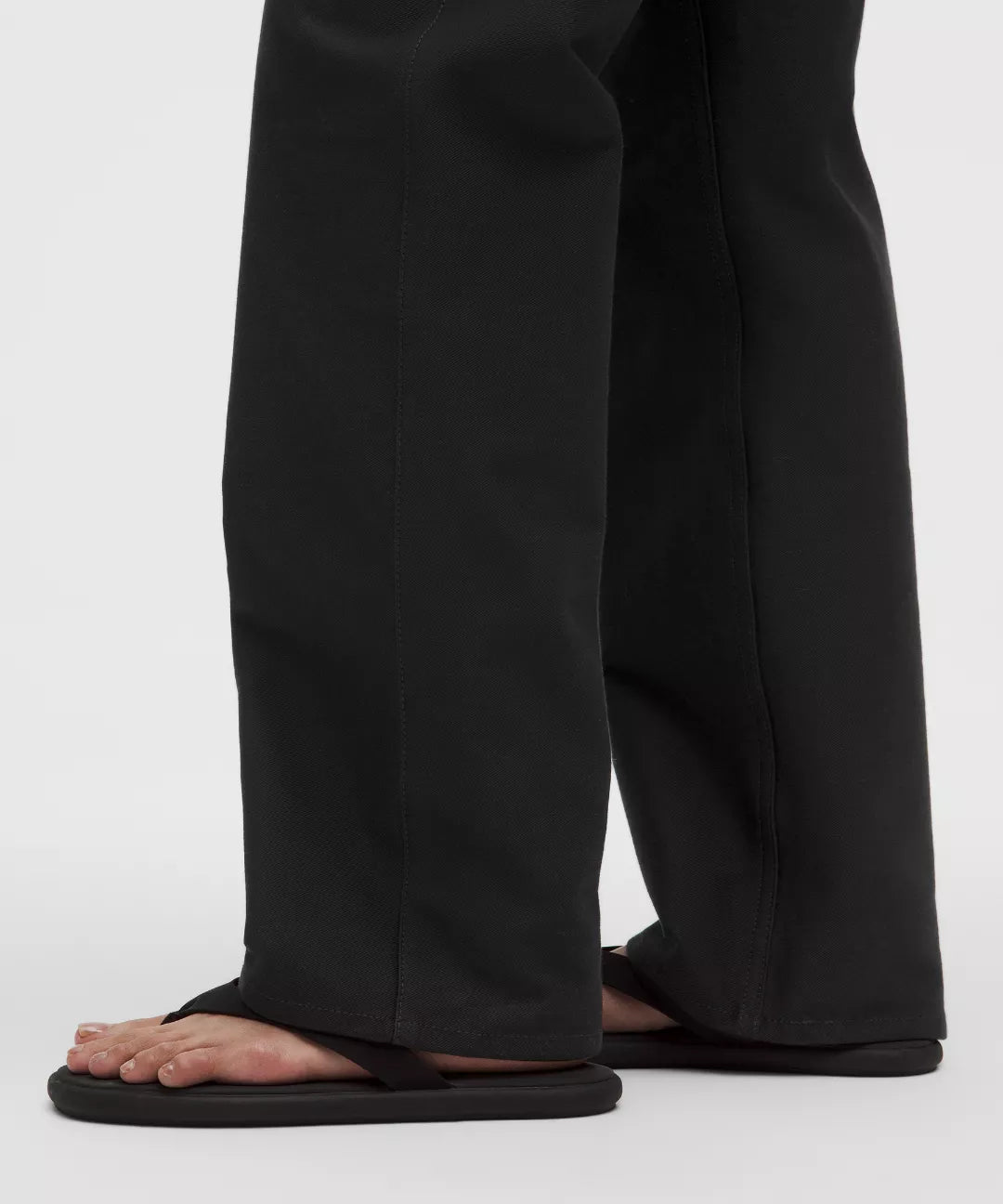 Person wearing black sandals and pants on a white background
