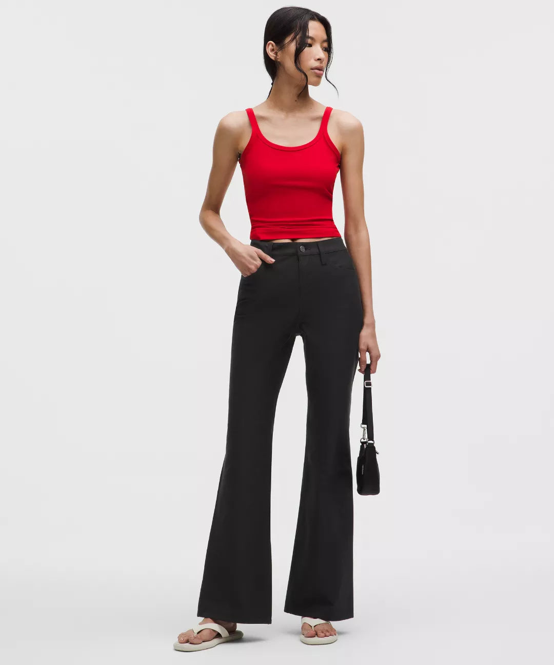 Woman wearing a red tank top and black flared pants on a white background