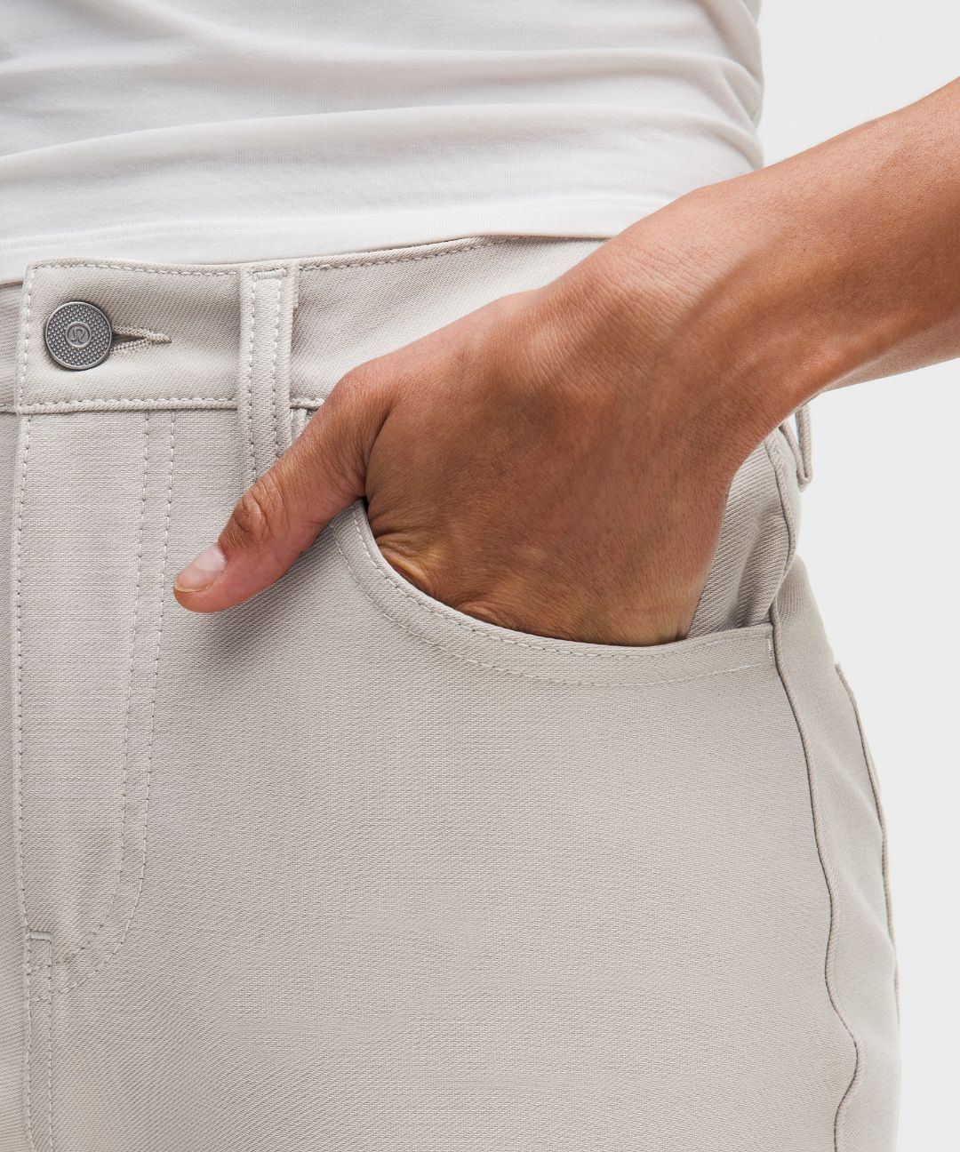 Close-up of a hand in a pocket of light-colored pants on a neutral background