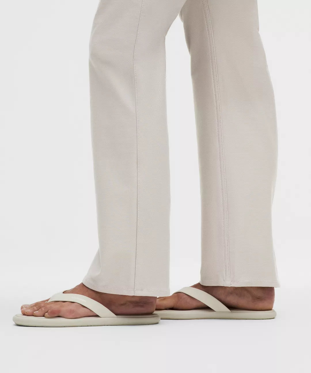 Person wearing light-colored sandals and beige pants on a white background