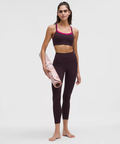 Woman holding a pink yoga mat wearing a dark sports bra and leggings on a white background